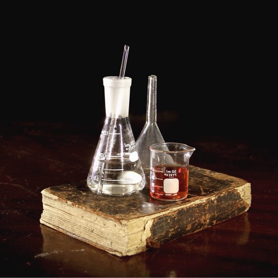 a grouping of glass flasks and beakers on top of an old, worn book