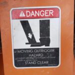 Caution sticker on heavy machinery, "Danger: Moving Outrigger Hazard, Stand Clear." Black and white illustration of a foot being flattened by the outrigger.